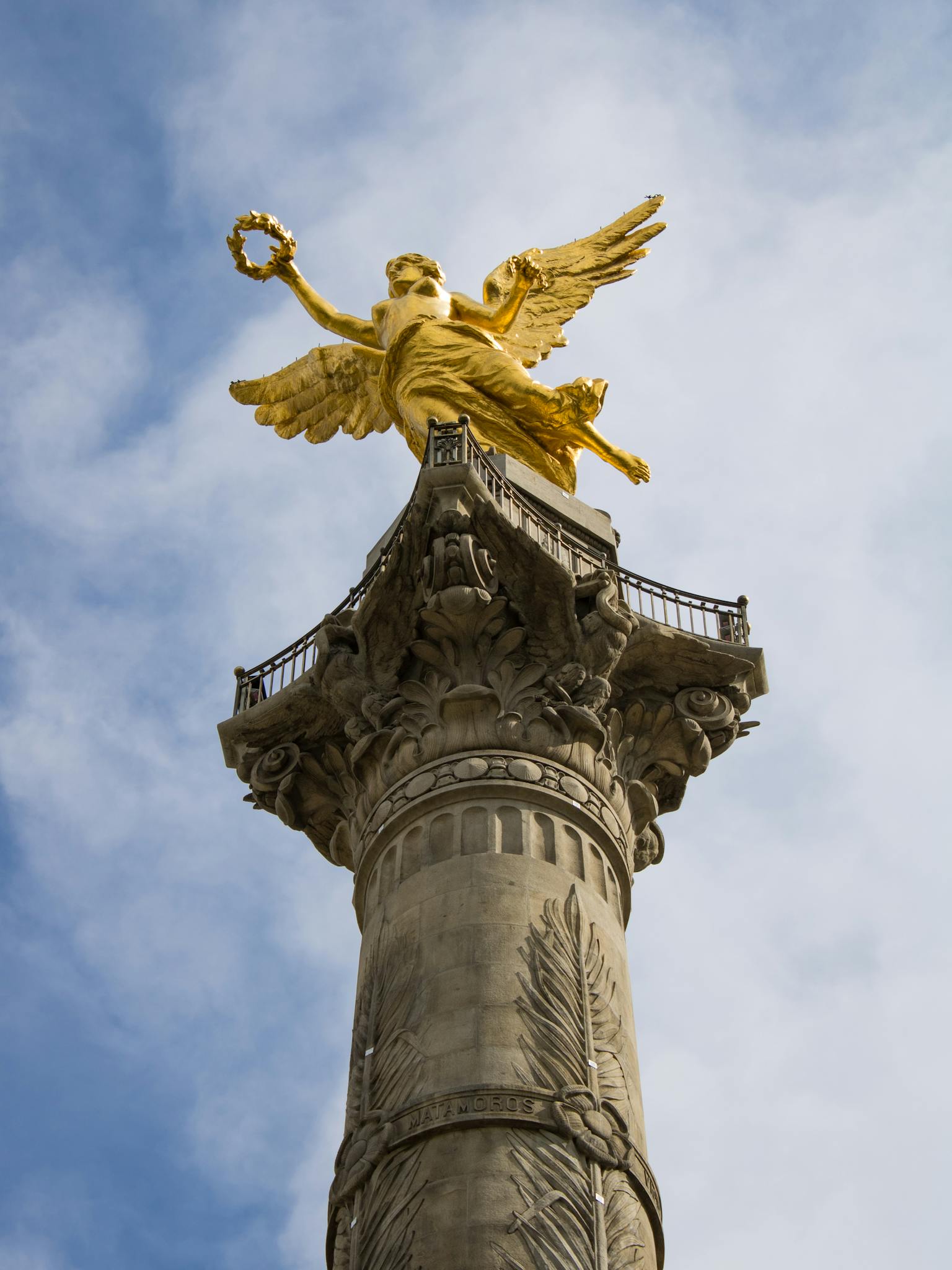 Low-angle view of the iconic Angel of Independence monument under a blue sky in Mexico City.
